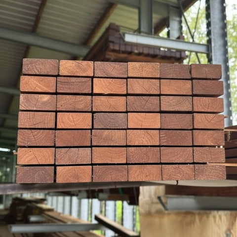 Een rechthoekige houten lat van bangkirai hout, 4-zijdig glad geschaafd, liggend op een houten ondergrond. De lat heeft een warme, bruinachtige kleur met een fijne houtnerf, kenmerkend voor bangkirai. Geschikt als onderstructuur voor gevelbekleding.