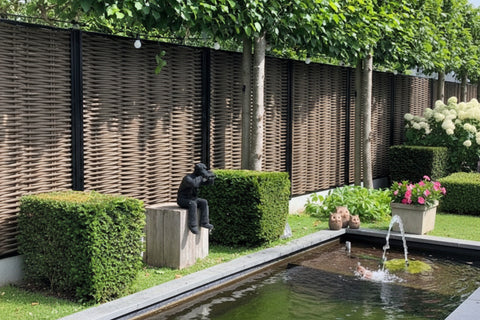 Luxe Forest Avenue fiber gevlochten tuinschermen met zwarte profielen in een moderne tuin met vijver, buxushagen en sfeerverlichting.
