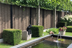 Luxe Forest Avenue fiber gevlochten tuinschermen met zwarte profielen in een moderne tuin met vijver, buxushagen en sfeerverlichting.